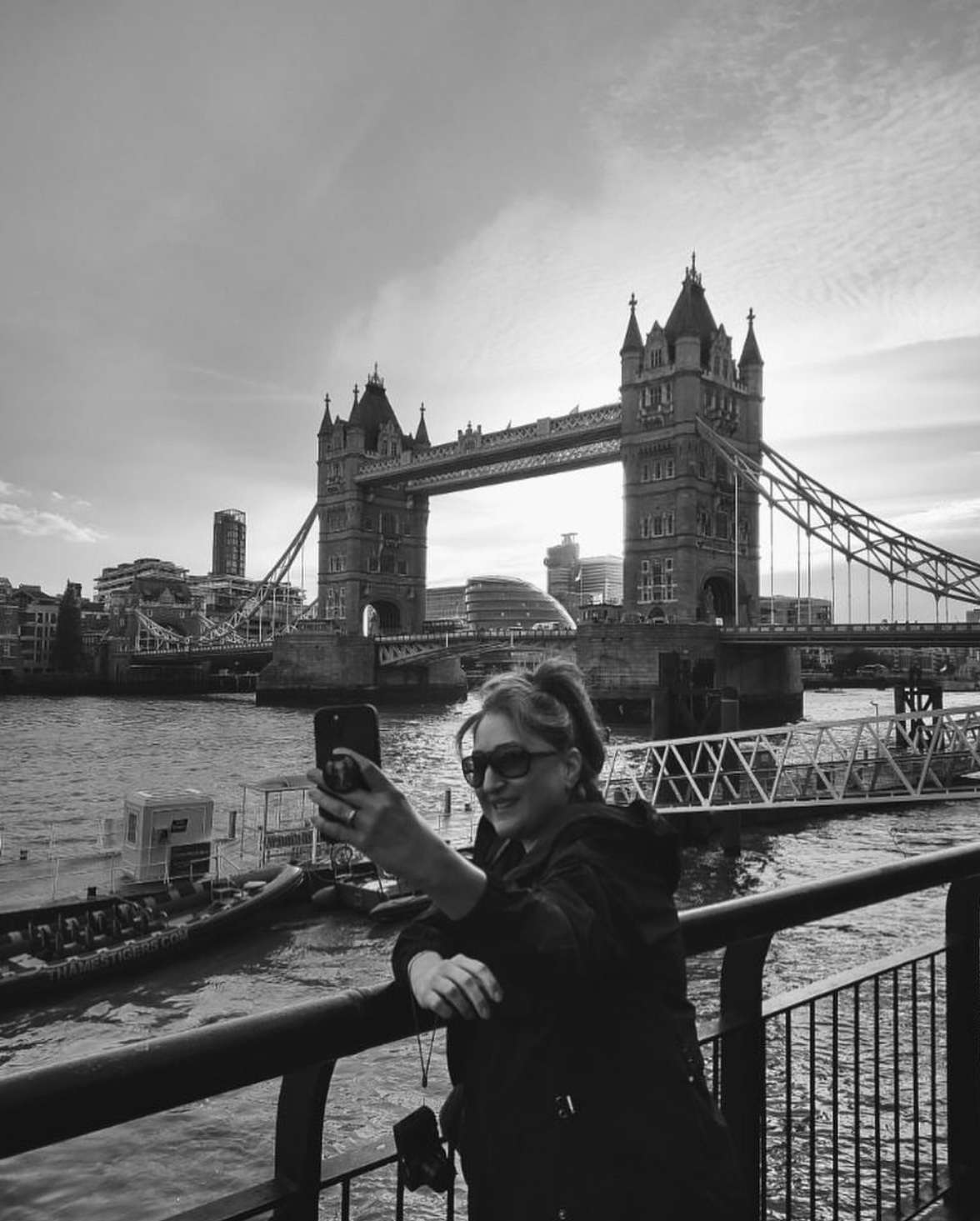 Bianca Marie Brookman | London Black and white photo of Bianca Brookman leaning against a railing on the Thames with London Bridge in the background.